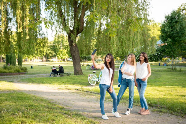 公園で3人の多民族の女の子が自撮りをしている。若い笑顔の女の子。全長 - 写真・画像