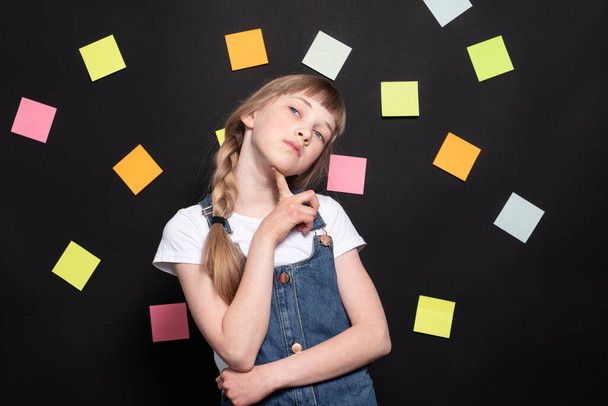 Ein Mädchen denkt über Aufgaben nach; viele Aufkleber auf schwarzem Hintergrund - Foto, Bild