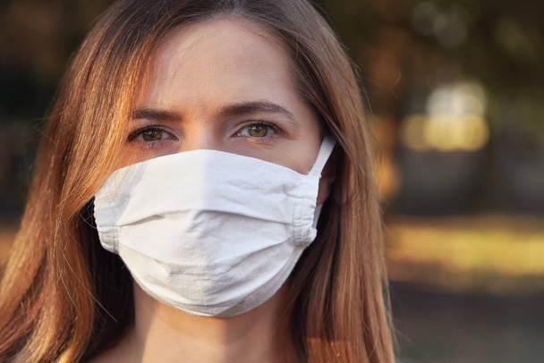 Young woman wearing white cotton virus mouth nose mask, nice bokeh in background, closeup face portrait - Foto, Imagen