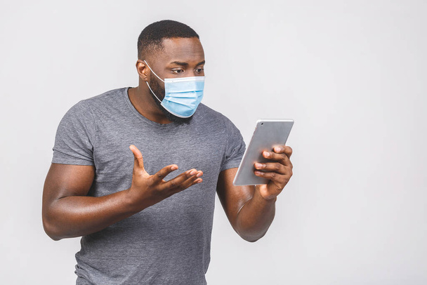 Медицинские новости! Африканский американец в медицинской стерильной маске держит цифровые таблетки изолированы на белом фоне.  - Фото, изображение
