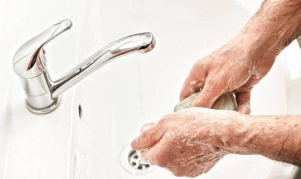 Senior elderly man his hands with soap under tap water faucet, detail photo. Can be used as hygiene illustration concept during coronavirus / covid-19 outbreak prevention - Fotó, kép