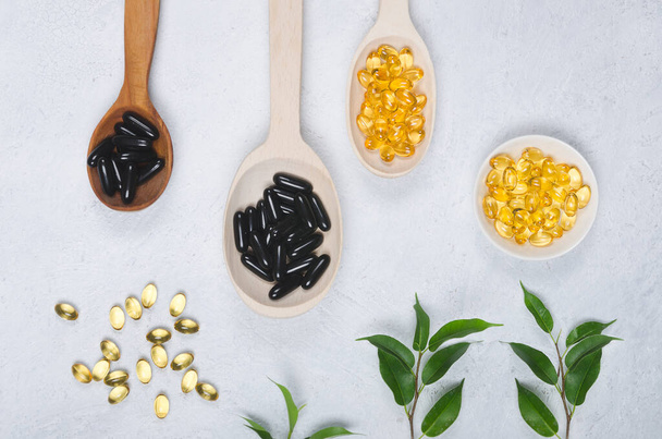 Black pills and yellow pill on wooden spoons on light background - Photo, Image