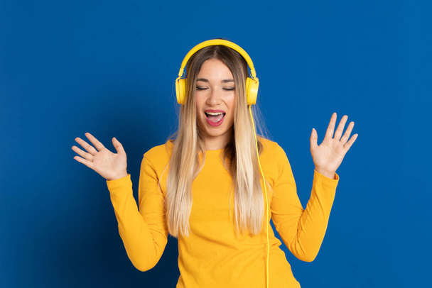 Blondýny dívka žlutá sluchátka na modrém pozadí - Fotografie, Obrázek