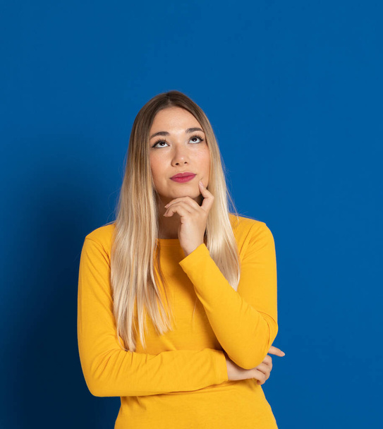 Blonde girl wearing a yellow T-shirt on a blue background - Photo, Image