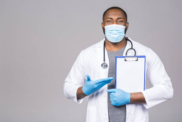 African american doctor man in face mask gloves isolated on grey background. Epidemic pandemic coronavirus 2019-ncov sars covid-19 flu virus. Holding clipboard. - Foto, afbeelding