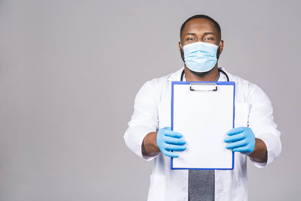 Африканский американский врач мужчина в перчатках в маске, изолированных на сером фоне. Эпидемический пандемический коронавирус 2019 года - вирус сарс ковид-19 гриппа. Холдинг буфер обмена. - Фото, изображение