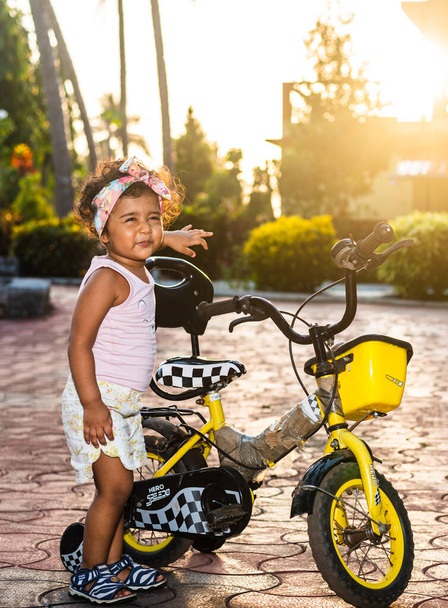 Speels mooi Indiaas meisje kind / baby / peuter dragen van een haarband, spelen met een cyclus / driewieler. Kind geeft vrolijke uitdrukkingen - Foto, afbeelding