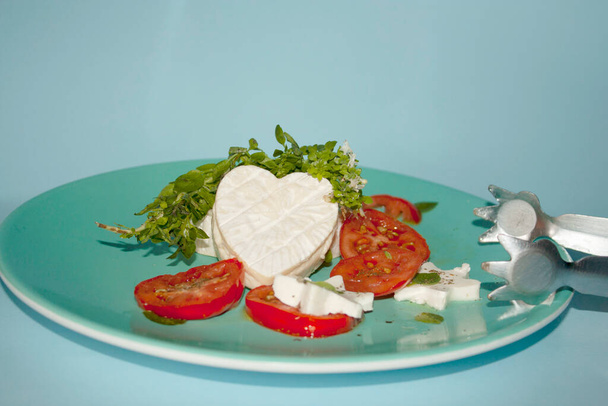 Fresh basil garnishing heart-shaped brie cheese on a salad plate with tomato slices and star-shaped panela cheeses - Foto, imagen