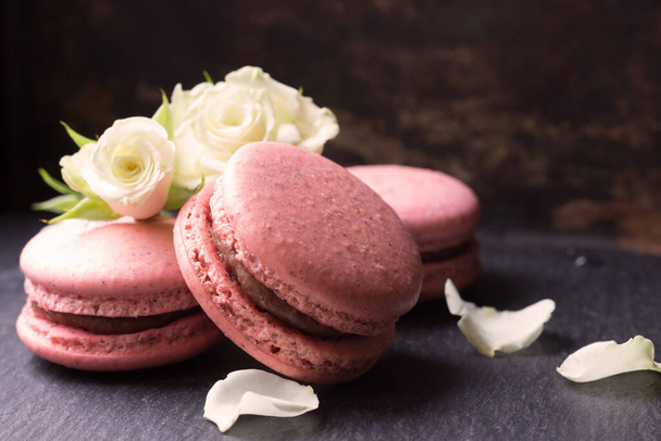 Pink Macaroons and white rose flowers  on dark background .French cookie - Photo, Image