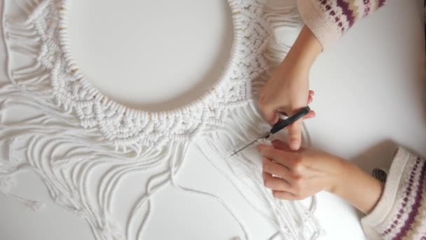 Boho style woman hands cutting circle wall hanging macrame with scissors on a white table - view from up above - Footage, Video