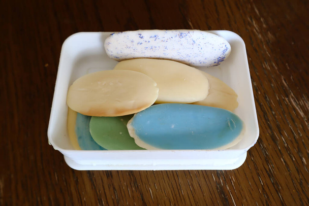 Diferentes sabonetes e restos em caixa de plástico branco na mesa de madeira lote de sabão sólido para higiene e limpeza.close-up, vista superior
  - Foto, Imagem