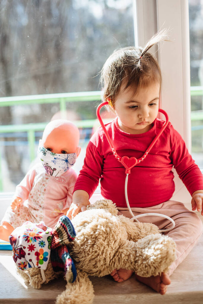 Девочка играет в доктора с игрушкой. Обучение детей профилактике ковида-19, вирусов и гриппа - Фото, изображение