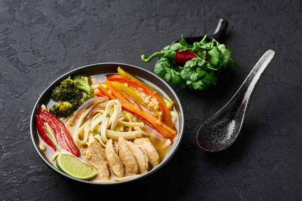 暗いスレートの背景に黒いボウルにチキントゥクパ。チキントゥクパは、野菜や鶏肉を使ったチベット料理の麺スープです。. - 写真・画像