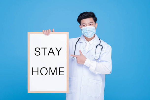 COVID-19検疫ロックダウン国。顔のマスクを身に着けているアジアの男性医師は、ホワイトボード「 STAY HOME 」を保持します, COVID-19コロナウイルスの流行の広がりを防ぐための隔離キャンペーン - 写真・画像