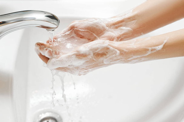 Hand Washing in white sink. Water flows from a faucet at soapy female hands. Covid-19 coronavirus protective measure. - 写真・画像