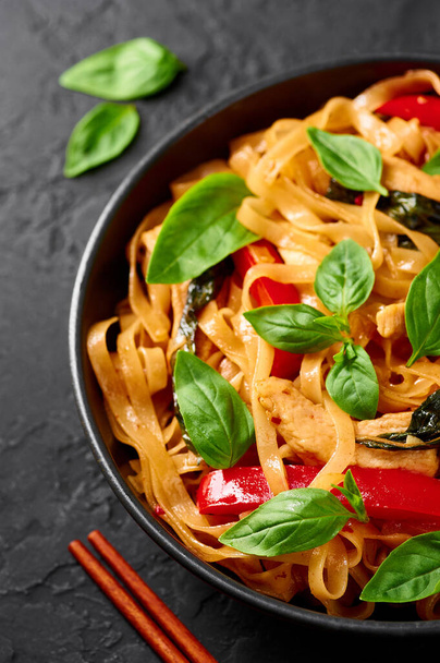 Thai Drunken Noodles or Pad Kee Mao in black bowl at dark slate background. Drunken Noodles is thai cuisine dish with Rice Noodles, Chicken meat, Basil, sauces and vegetables. Thai Food. Close up - Photo, Image