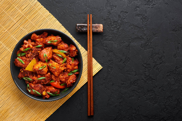 Ψάρια Manchurian ξηρό μοιάζει με Schezwan Ψάρια σε μαύρο μπολ σε σκούρο φόντο σχιστόλιθο. Fish Manchurian - είναι ινδικό κινέζικο πιάτο κουζίνας με βαθύ τηγανητό σολομό, πιπεριές, σάλτσα και κρεμμύδι. Άνω όψη. - Φωτογραφία, εικόνα