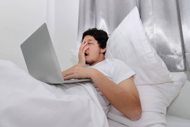 Concepto de gente trabajadora. Cansado de exceso de trabajo joven asiático durmiendo con ordenador portátil en la cama en el dormitorio
. - Foto, imagen