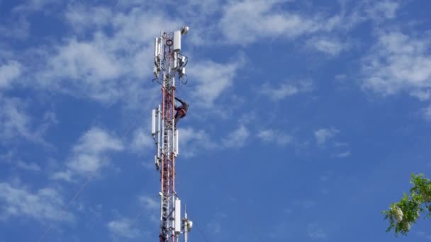 Een zendmast met cellulaire antennes tegen een blauwe lucht. Een werktuigbouwkundige voert werkzaamheden uit om problemen op grote hoogte op te lossen. 5e generatie mobiele communicatie. - Video