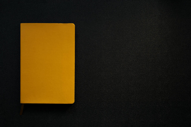 Желтый блокнот на черном кожаном фоне. Блокнот в левом углу. желтый прямоугольник на черном фоне
 - Фото, изображение