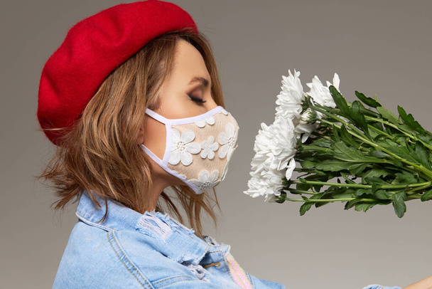 Woman in trendy fashion outfit during quarantine of coronavirus outbreak with flowers. Model dressed protective stylish handmade face mask and red beret - Photo, Image