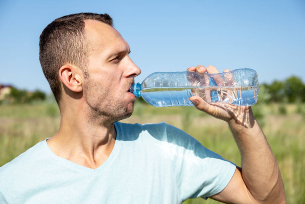 молодий чоловік п'є воду з пляшки в природі
 - Фото, зображення