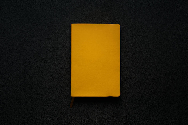 žlutý zápisník na černém koženém pozadí. Zápisník uprostřed - Fotografie, Obrázek
