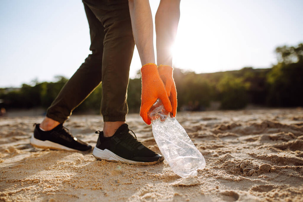 Jovem voluntário pega lixo plástico na costa oceânica. Um homem recolhe resíduos à beira-mar para salvar a ecologia e proteger o meio ambiente. Reciclar lixo e conceito de poluição
 - Foto, Imagem