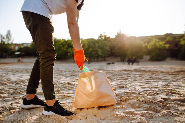 Młody ochotnik odbiera plastikowe śmieci na wybrzeżu oceanu. Człowiek zbiera odpady na wybrzeżu, by ratować ekologię i środowisko. Koncepcja recyklingu odpadów i zanieczyszczeń - Zdjęcie, obraz