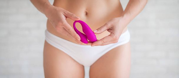 A faceless woman in white panties holds a curved pink clitoral vaginal vibrator. Female sex toy for masturbation. Self-gratification. Demonstrates dildo. - Foto, Imagen