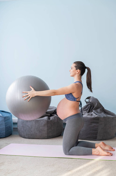 Pregnant european woman performs exercises with fitness ball. Expectant mother is doing yoga in the 3rd trimester. Girl in the classroom in preparation for childbirth. - Foto, Bild