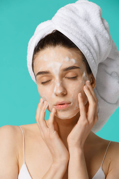 Young woman with towel wrapped around her head applying facial cleaning foam and having fun. Daily routine - face cleaning, skin care, peeling, moisturising and beauty treatment concept - Fotografie, Obrázek