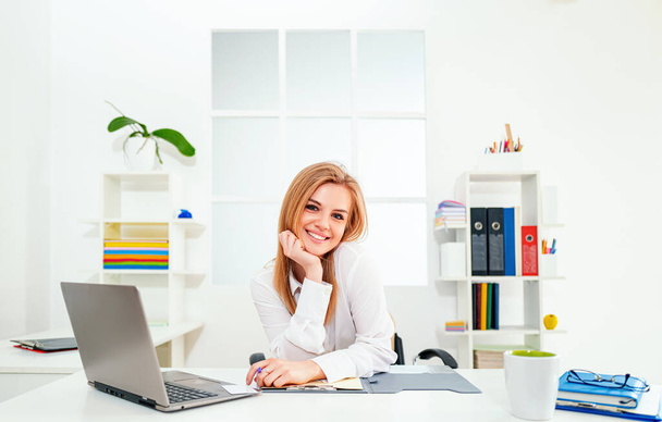 Young smiling business woman in white modern office. Beauty secretary. Beautiful young woman working with laptop in office. - Foto, Imagen