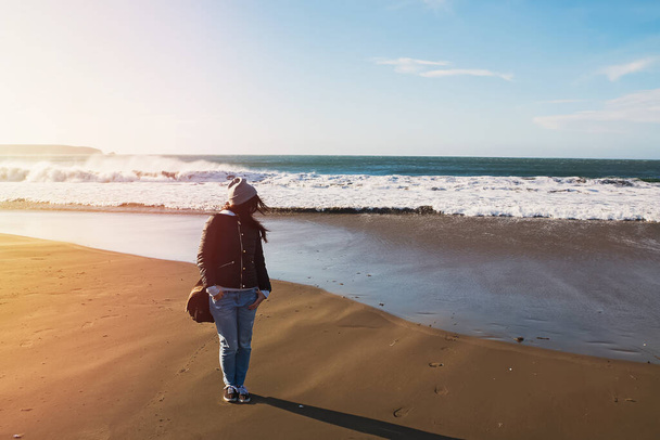 Woman in a hat walking on Pacific ocean coast on windy day - Photo, image
