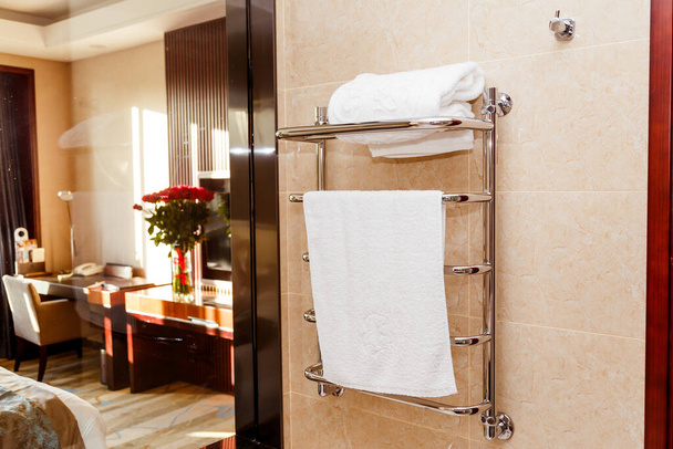 Moderne verwarmde handdoekhouder op betegeld in hotel. - Foto, afbeelding