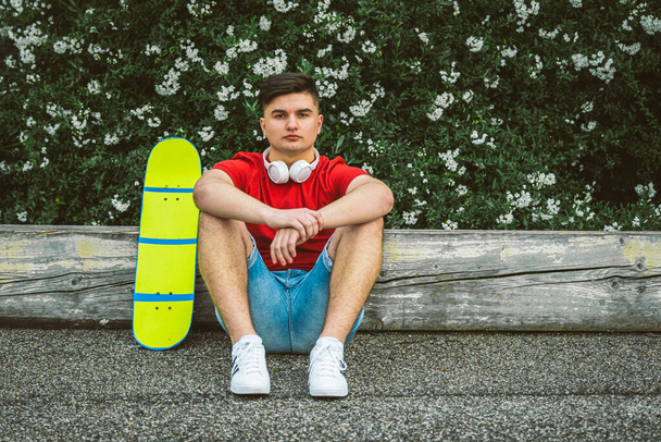 Teen Boy is sitting resting with Longboard - Young adults outdoor skating - A young guy is sitting with a longboard - Portrait of beautiful boy skater - Foto, Imagem