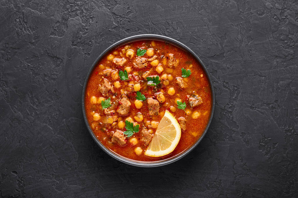 モロッコハリラ暗いスレートの背景に黒いボウルにスープ。ハリラは、子羊や牛肉の肉、ひよこ豆、レンズ豆、トマトとチリアントロとモロッコ料理です。ラマダーン・イフタール料理。トップ表示 - 写真・画像