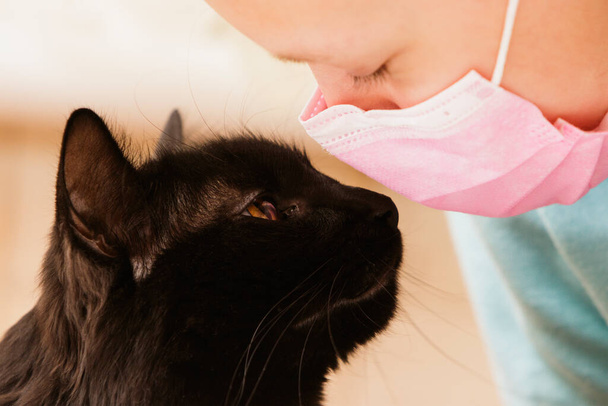 Girl in medical mask alone at home communicates with favorite pet - Fotografie, Obrázek