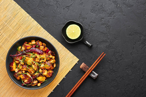 Kung Pao Paneer na černém břidlicovém pozadí. Kung Pao Paneer je vegetariánská verze čínského sichuan jídlo Gong Bao s paneer sýr, arašídy, chilli papričky, omáčky a cibule. Horní pohled. Kopírovat prostor - Fotografie, Obrázek