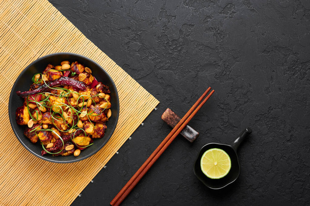 Kung Pao Paneer auf schwarzem Schiefergrund. Kung Pao Paneer ist eine vegetarische Version des chinesischen Sichuan-Gerichts Gong Bao mit Paneer-Käse, Erdnüssen, Chilischoten, Soßen und Zwiebeln. Ansicht von oben. Kopierraum - Foto, Bild