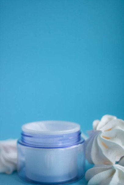 Hermoso frasco de crema azul con merengues sobre un fondo azul
 - Foto, Imagen