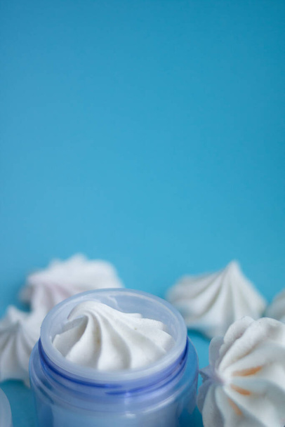 Hermoso frasco de crema azul con merengues sobre un fondo azul
 - Foto, Imagen