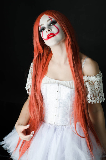 een meisje in een clown kostuum met eng make-up op een zwarte achtergrond - Foto, afbeelding