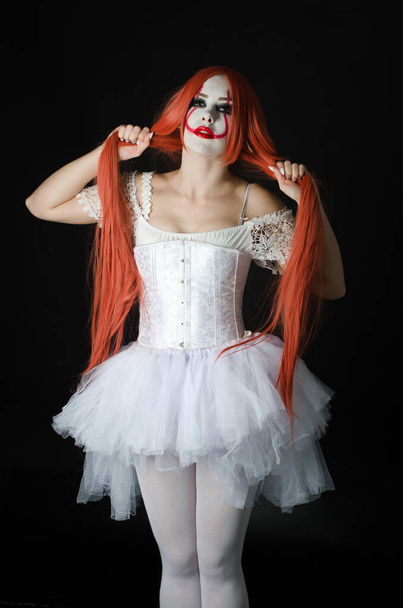 uma menina em um traje de palhaço com maquiagem assustadora em um fundo preto
 - Foto, Imagem