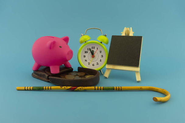 Saving for old-age and retirement concept with open purse with coins, walking stick, alarm clock and piggy bank over a blue background with copy space - Photo, Image