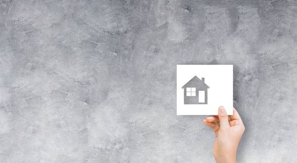 Real Estate and Housing Concept: Mão segurando símbolo ícone de papel casa com parede de concreto fundo textura grunge
. - Foto, Imagem