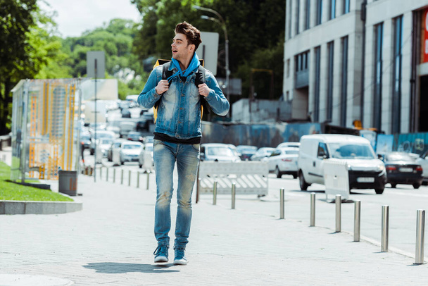Zusteller mit Rucksack läuft auf Stadtstraße neben Straße  - Foto, Bild