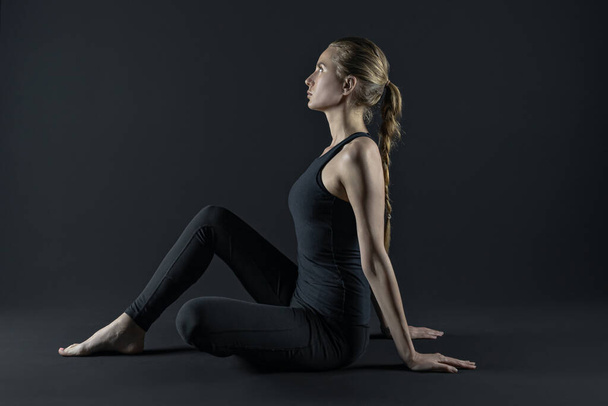 Junge Frau praktiziert Yoga-Positionen. Sport Workout Fitness-Übung. Yogamatte und Leggins auf dunkelschwarzem Hintergrund. - Foto, Bild