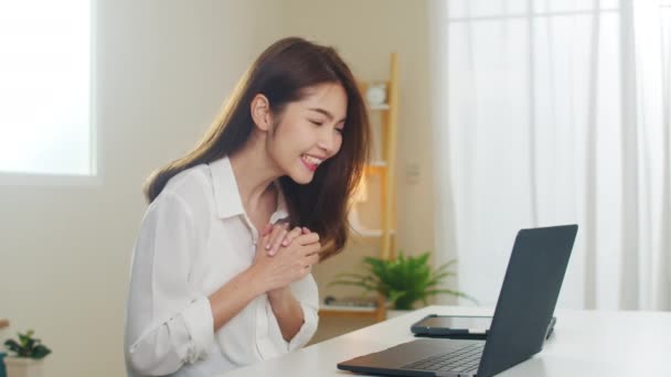 Fiatal ázsiai üzletasszony laptopos videohívással beszél párral, miközben otthonról dolgozik a nappaliban. Önizoláció, társadalmi távolság, karantén a koronavírus számára a következő normális koncepcióban. - Felvétel, videó