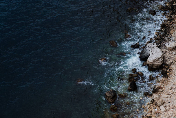 Festői kilátás sziklás sziklákkal, kövekkel, tengeri öböllel. Veszélyes tengeri hullám zuhan le a szikla partján spray-vel és habbal vihar előtt - Fotó, kép